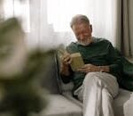 Senior man relaxing and reading a book on a sofa, enjoying the cozy holiday atmosphere indoors.