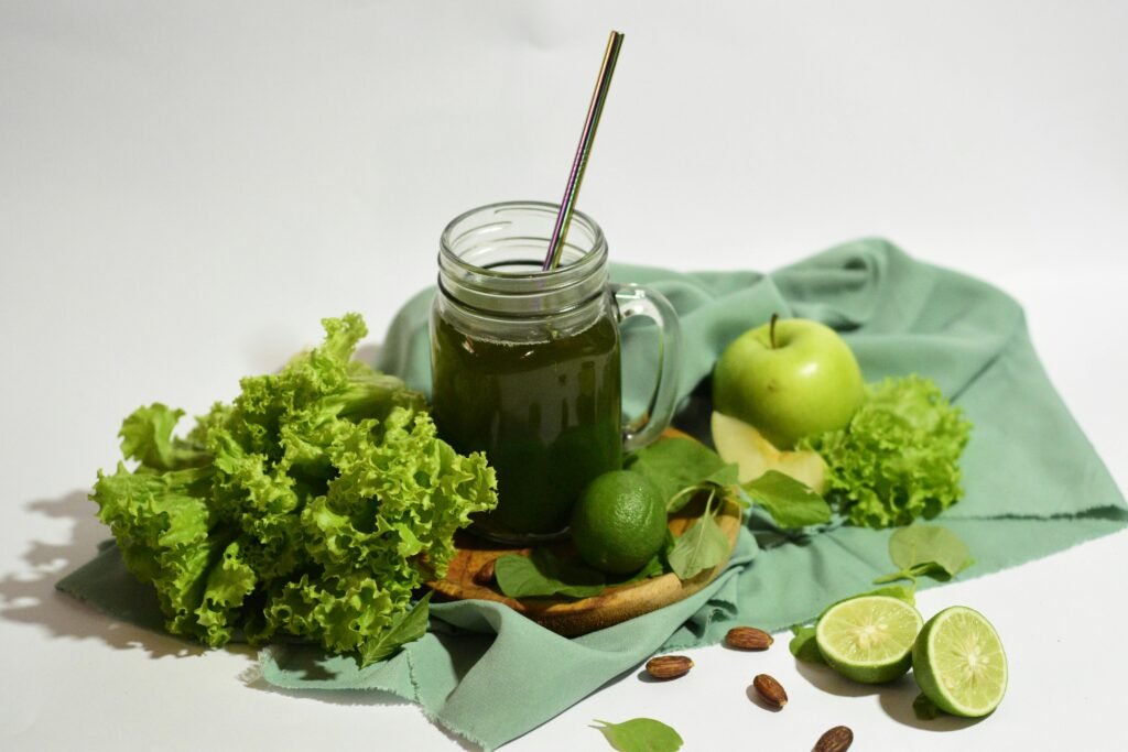A vibrant green juice surrounded by fresh apples, limes, and lettuce, served in a mason jar with a metal straw.