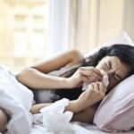A woman lying in bed sneezing,shows signs of spring allergies, such as watery eyes and a stuffy nose.