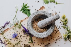 Stone mortar filled with assorted spices and fresh herbs, with more spices scattered nearby, showing simple Ayurvedic kitchen ingredients for natural wellness.