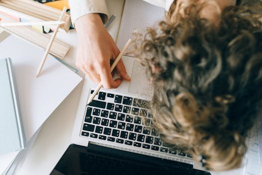 An exhausted employee overwhelmed with work, resting on a laptop and papers.