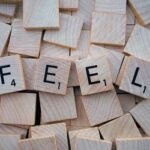 Close-up of Scrabble tiles spelling 'Feel' scattered on a wooden background.